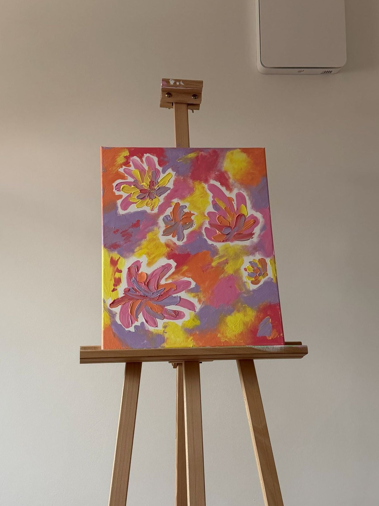 Colorful floral painting on an easel against a white wall.