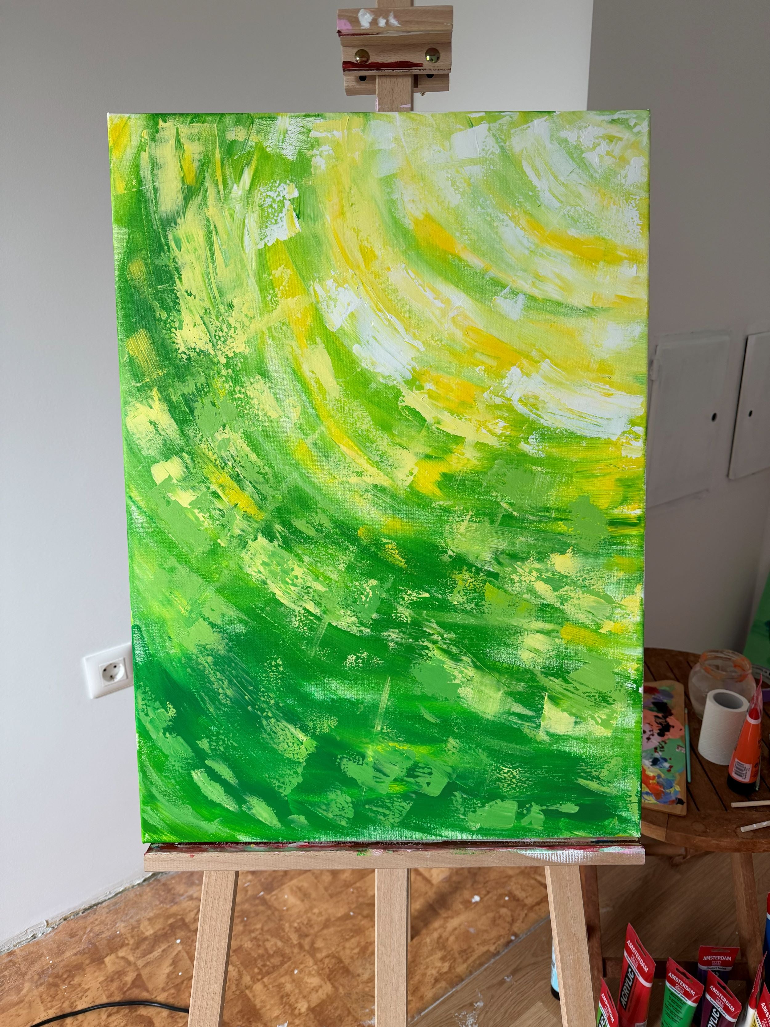 Abstract painting on a canvas with swirling green and yellow patterns, displayed on an easel.