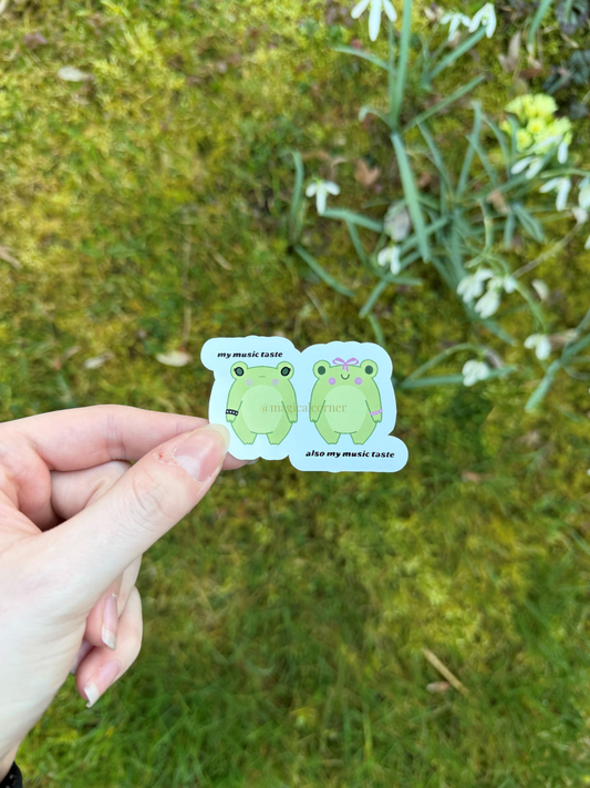 Two frog stickers held by a hand with a natural background